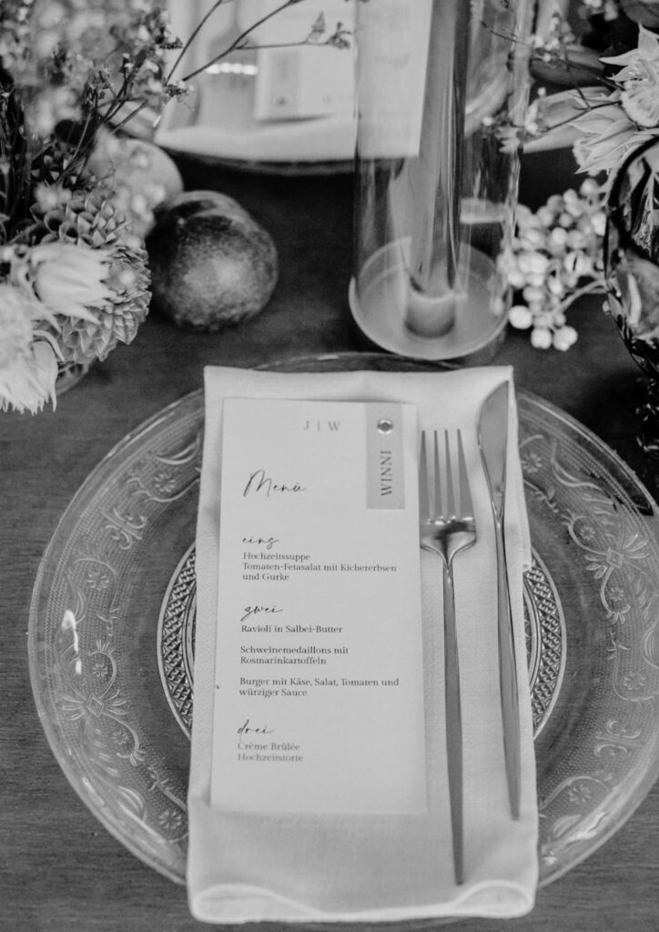 Gedeck einer Hochzeitstafel mit Menükarte, Glas und floraler Dekoration